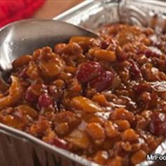 a close up of a spoon in a tin pan filled with baked beans and cranberries