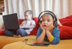 a little boy laying on the floor with headphones and looking at a laptop computer