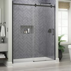 a walk in shower next to a white toilet and bathtub with grey tile on the walls