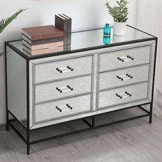 a silver dresser with drawers and books on top next to a potted green plant