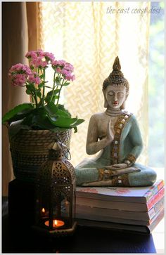 a buddha statue sitting on top of a stack of books next to a potted plant