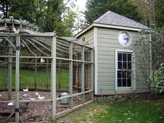 a small chicken coop in the middle of a yard next to a building with a clock on it's side