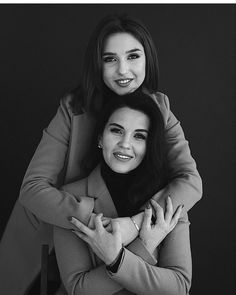 two women are hugging each other in black and white, one is wearing a coat