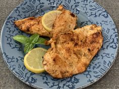 two pieces of chicken on a blue plate with lemon wedges and spinach leaves