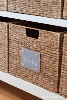 two wicker baskets with labels on them sitting on top of a white dresser drawer