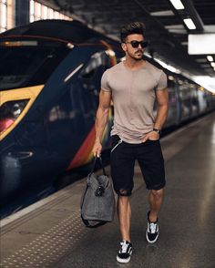 a man with sunglasses is standing in front of a train and holding a handbag