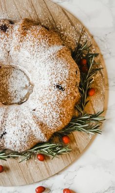 a cake with powdered sugar and rosemary sprinkled on top sits on a wooden platter