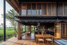 a wooden deck with chairs and table next to an open air kitchen on the other side