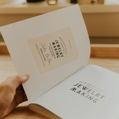 a person holding an open book on top of a wooden table