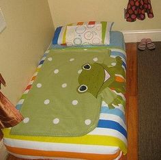 there is a bed with a green dinosaur blanket on it and two stuffed animals hanging from the wall