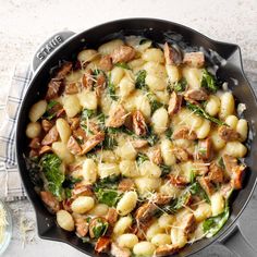 a skillet filled with pasta and spinach on top of a white tablecloth