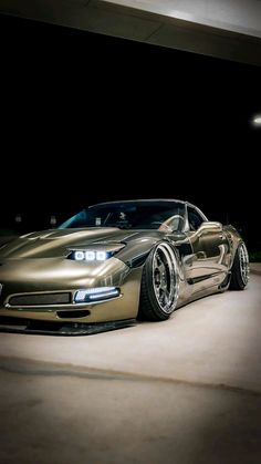 a gold sports car parked in a parking lot at night with the headlights turned on