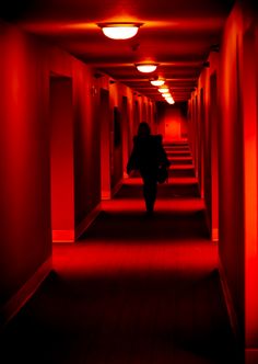 a person walking down a long hallway with red lights