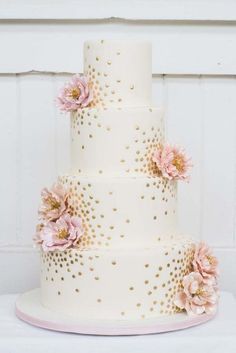 a three tiered cake with pink flowers and gold polka dots on the bottom layer