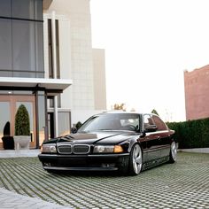 a black car parked in front of a building on a brick driveway with grass and bushes behind it