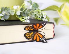 an orange and black butterfly sitting on top of a book next to some white flowers