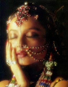 a woman with her hands on her face and jewelry around her neck, wearing an elaborate headdress