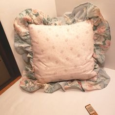 there is a pillow on the bed with a flowered ruffle around it and a remote control next to it