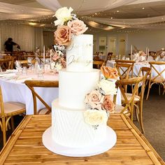 a three tiered wedding cake with flowers on the top is sitting on a table