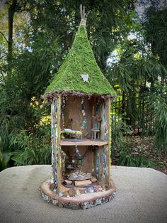 a bird house with moss growing on it's roof and shelves in front of trees