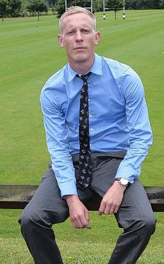 a man in a blue shirt and tie is sitting on a park bench with his legs crossed