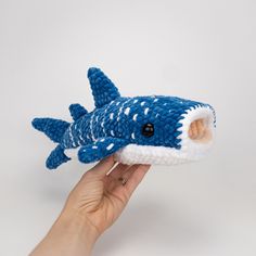 a hand is holding a blue and white knitted toy that looks like a shark