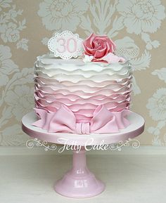 a pink and white tiered cake with flowers on top