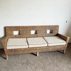 a wicker couch with four cushiones on the back and sides, in front of a white wall