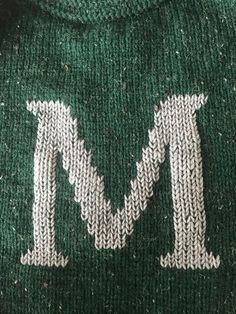 the word m is written in white on a green sweater