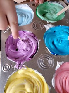 a person is dipping colored icing into a muffin tin