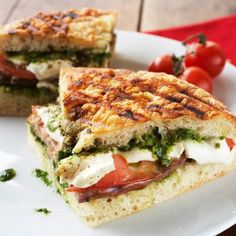 a sandwich cut in half sitting on top of a white plate next to tomatoes and lettuce