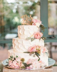 a white wedding cake with pink flowers on top and mr and mrs written on the side