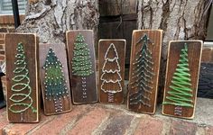 four wooden signs with different designs on them sitting next to a tree and brick walkway