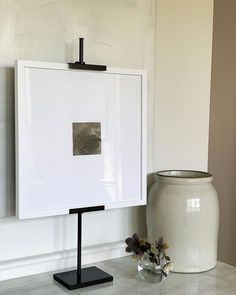 a white vase sitting on top of a table next to a framed piece of art