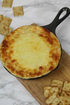 a cheese pizza sitting on top of a wooden cutting board next to crackers