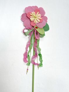 a pink flower with green leaves and ribbons