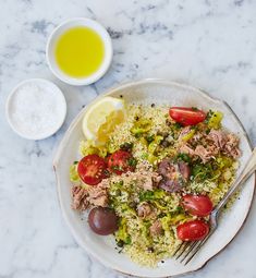 a white plate topped with meat and rice next to a bowl of olives, tomatoes and lemon wedges