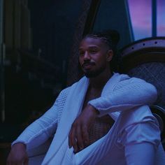 a man sitting on top of a chair wearing a white robe and holding his hands in his pockets