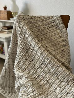 a chair with a blanket on top of it in front of a table and bookshelf