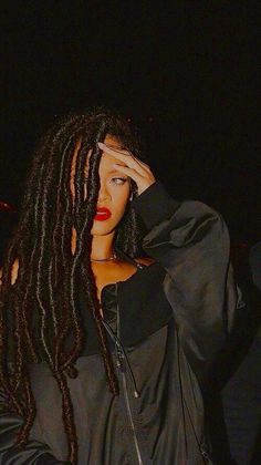 a woman with long dreadlocks is holding her hand up to her face and looking at the camera