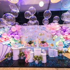 a table topped with lots of balloons next to a wall covered in mermaid tail decorations