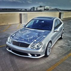 a silver car parked on top of a parking lot next to a tall building and cloudy sky