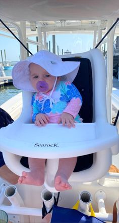 a baby sitting in a highchair on a boat wearing a sun hat and blue shirt