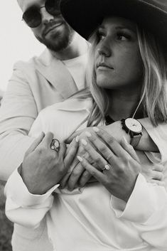 a man and woman standing next to each other with their hands on the chest, both wearing rings