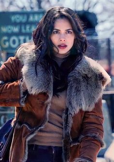 a woman walking down the street with her hand on her hip and wearing a fur collared coat