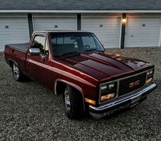 a maroon pick up truck parked in front of a garage