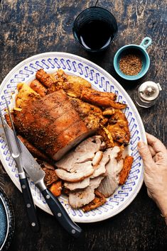 a person is holding a knife and fork near a plate with roast meat on it