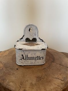 an old fashioned white box sitting on top of a tree stump with the word allumetes written on it