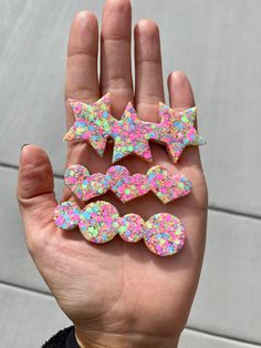 a hand is holding five decorated cookies with sprinkles in the shape of bows