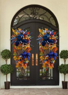 two large wreaths with flowers on them hang from the front door of a house